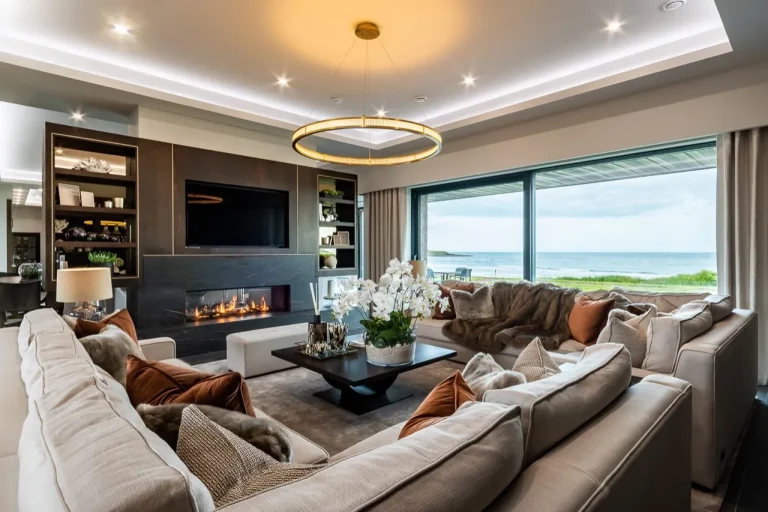 Sea-view sitting room at Camelot Waterford in Ardmore, with sofas, a fireplace and windows overlooking the coast