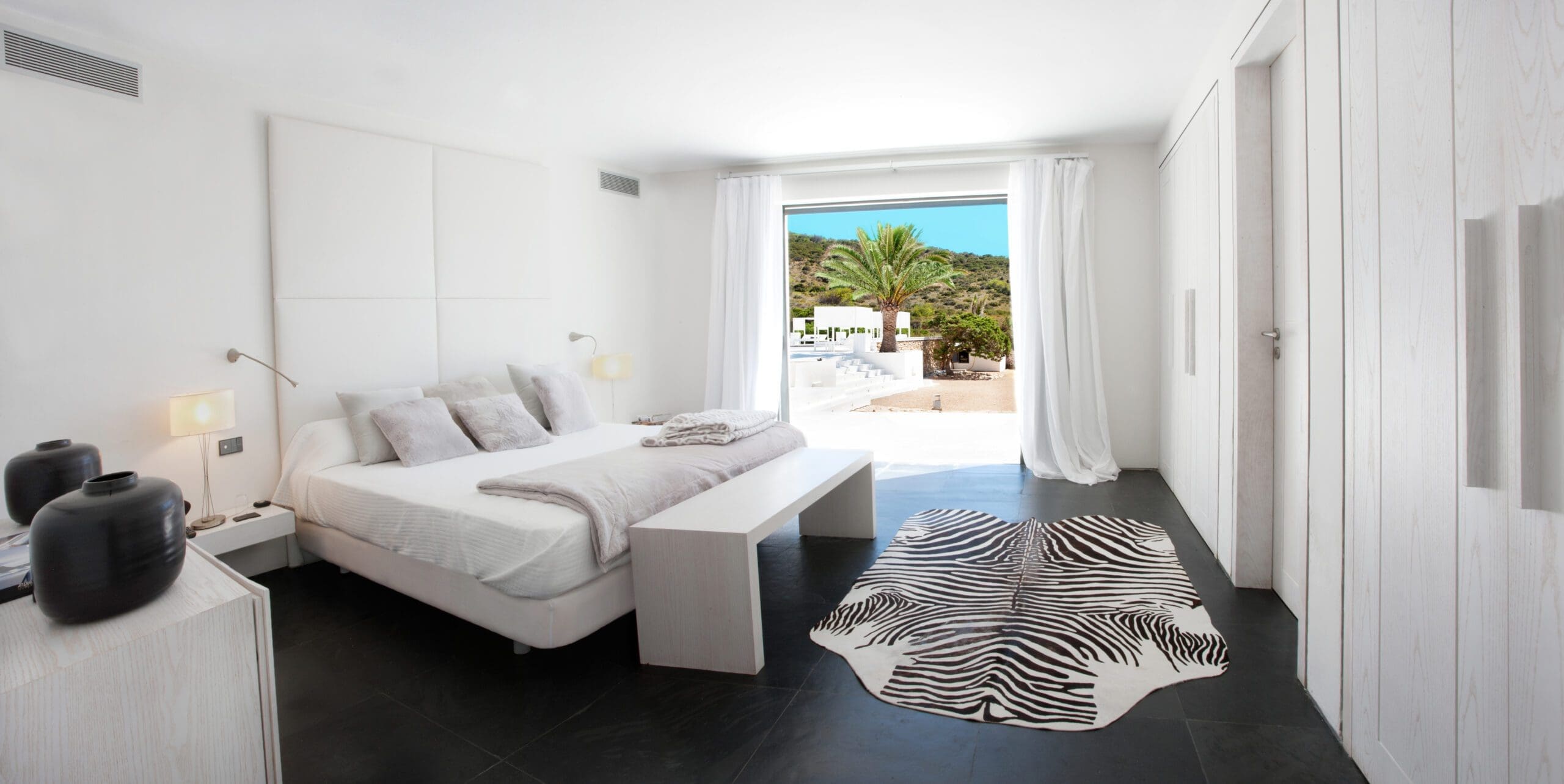 Tagomago bedroom with white furnishings and sliding doors opening to a garden terrace