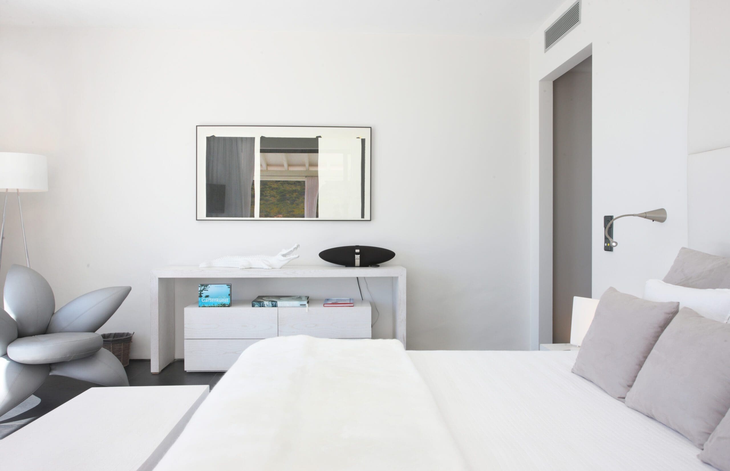Tagomago bedroom with white walls, grey furnishings and an armchair