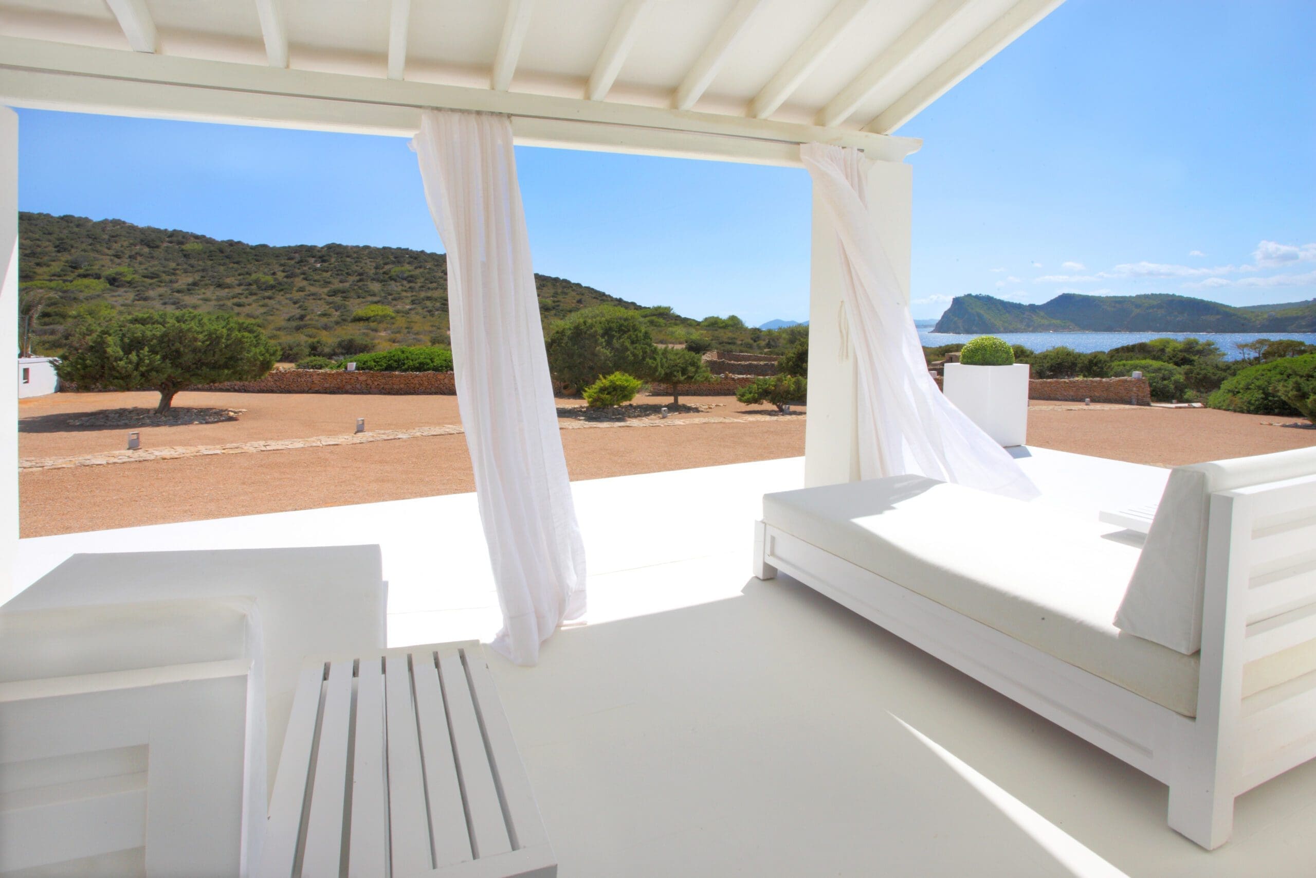 Covered Tagomago terrace with white seating overlooking island vegetation