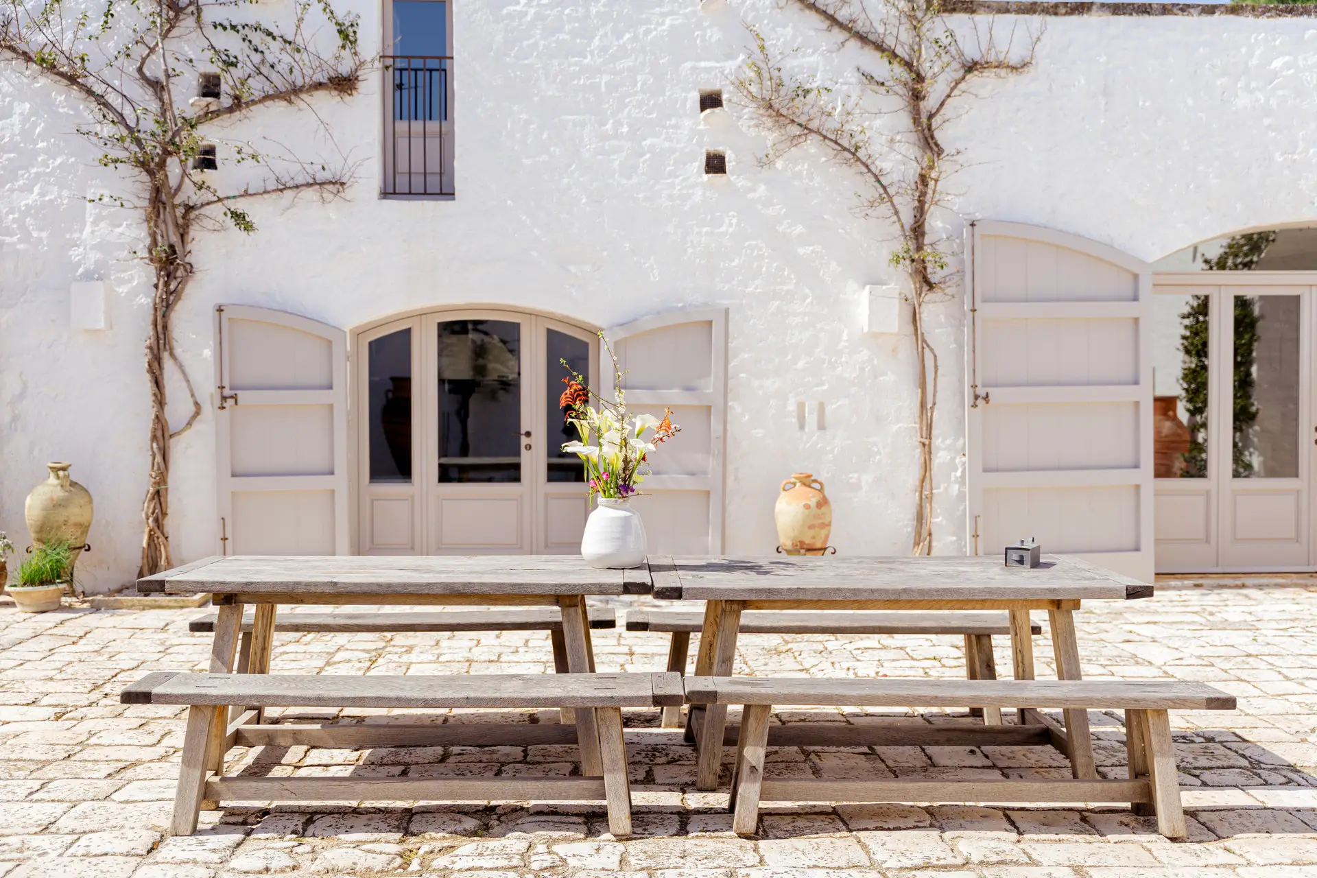 Long wooden dining table and benches in the white stone courtyard at Masseria Petrarolo
