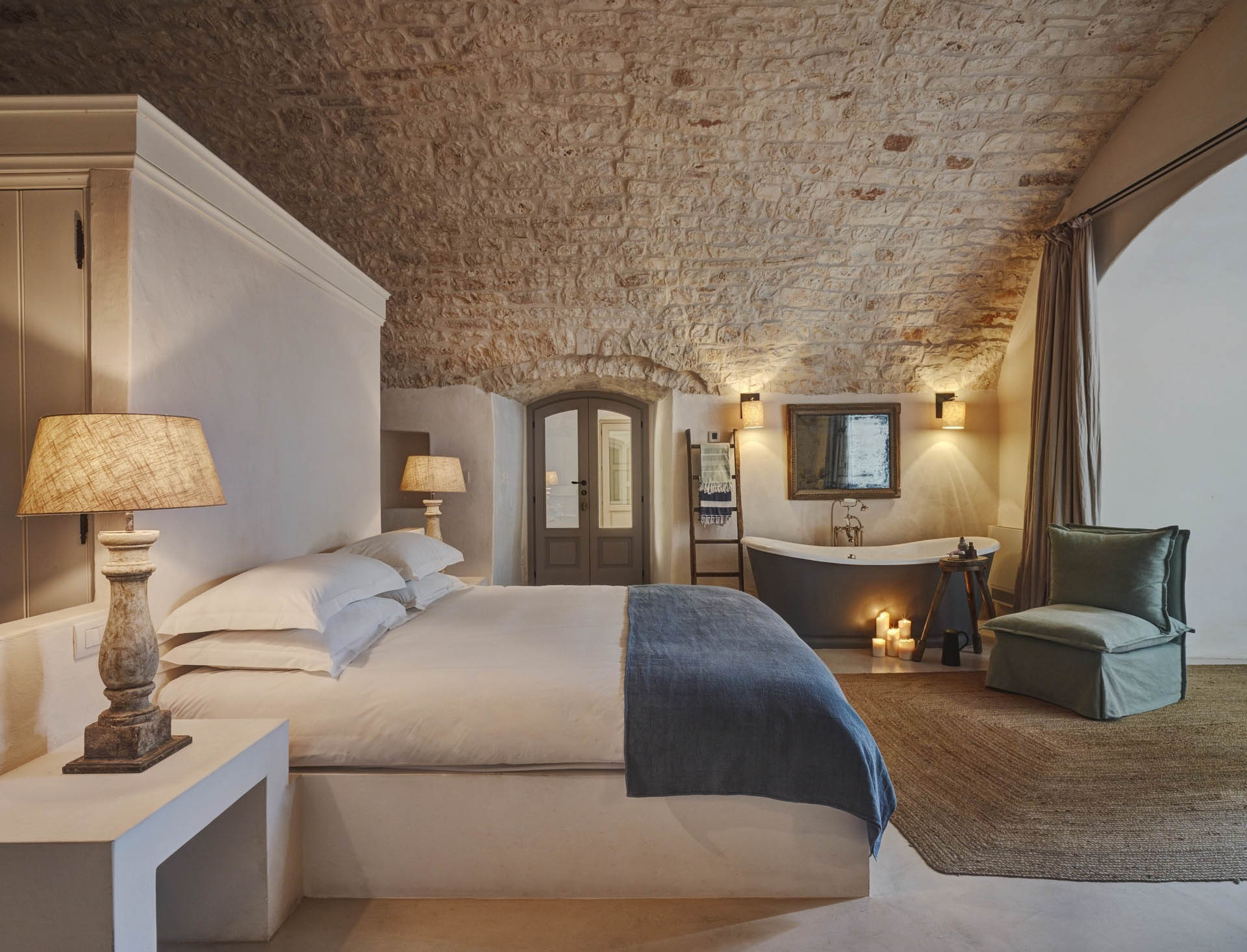 Bedroom at Masseria Petrarolo with a vaulted stone ceiling, pale bedding and a freestanding bath