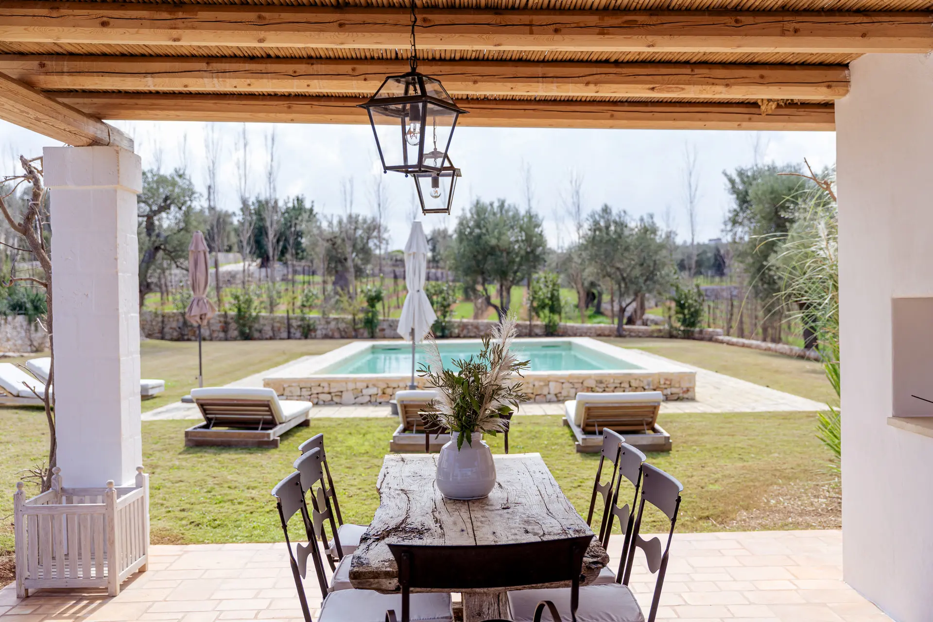 Covered dining terrace at Trullo Petrarolo with the private pool and olive countryside beyond