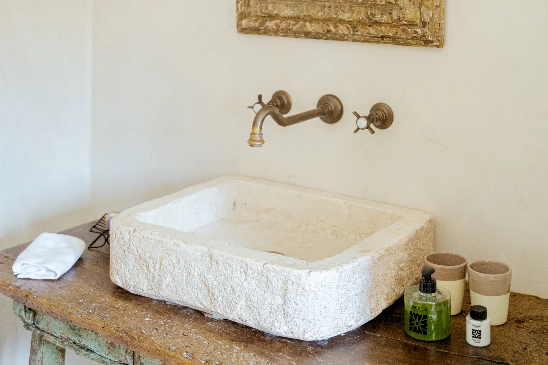Carved stone bathroom basin and wall-mounted brass taps at Trullo Petrarolo